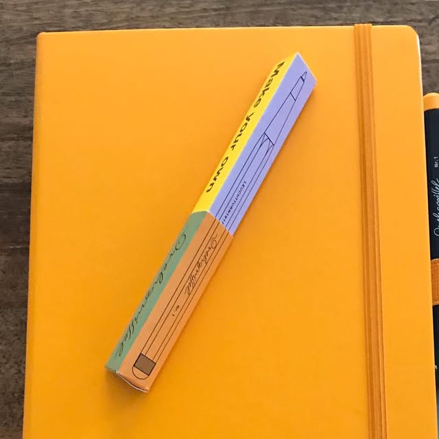 Un carnet Leuchtturm1917 orange et la boîte d'un stylo Drehgriffel posés sur une table en bois