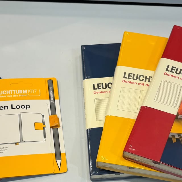 Trois carnets Leuchtturm1917, bleu marine, jaune et rouge, à côté d'un Pen Loop jaune